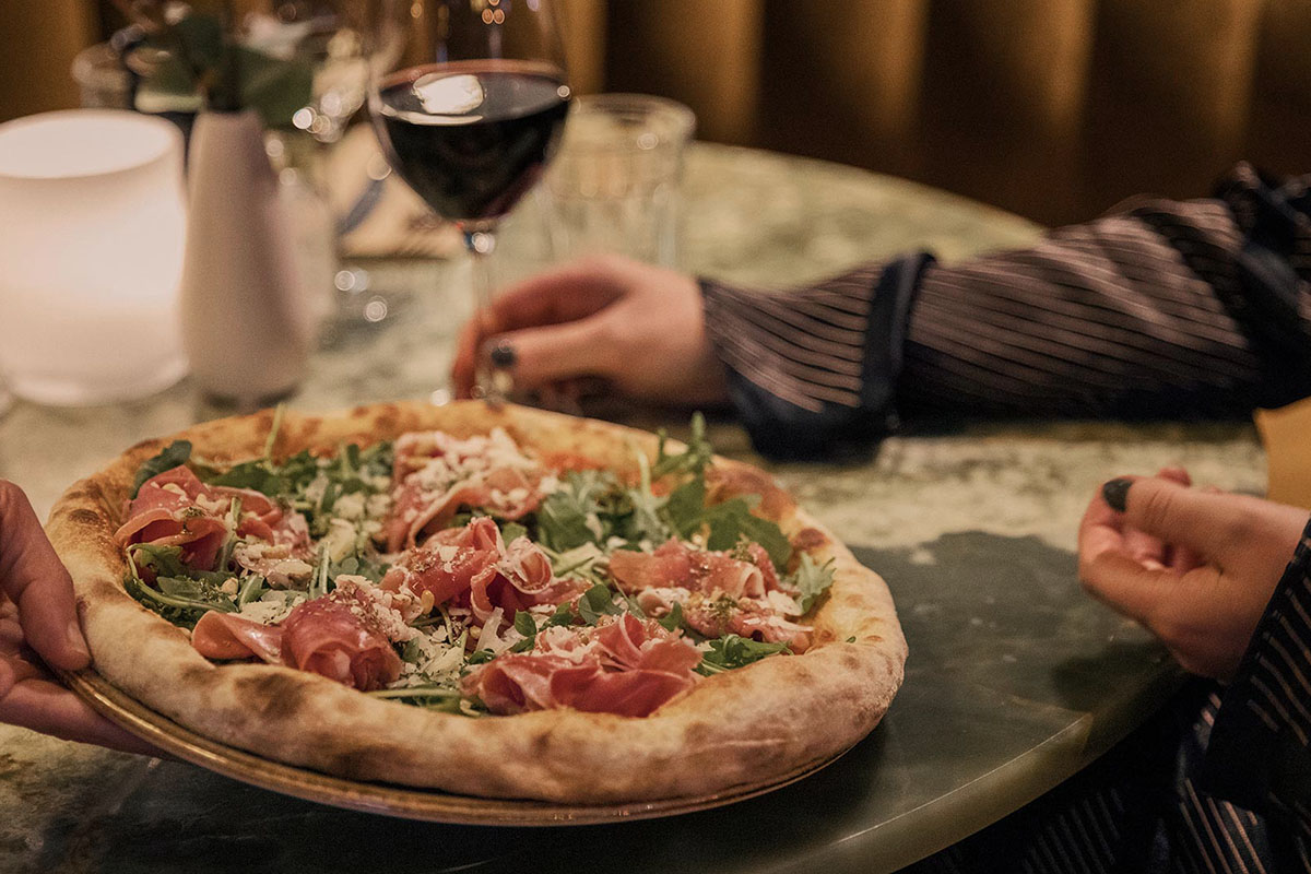 Pizza med lufttorkad skinka och ruccola serverad med ett glas rödvin på Corner.